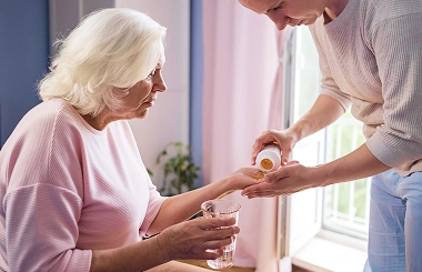 Caregiver giving medication to elderly woman