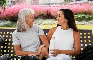 Smiling elderly woman sitting on bench with younger woman