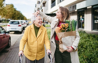 Elderly woman walking with caregiver carrying groceries