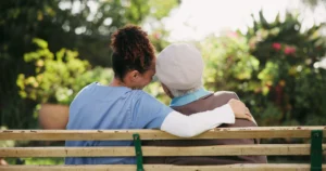 Compassionate caregiver sharing a comforting moment with an elderly woman outdoors.