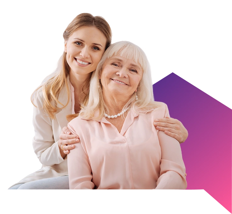 Two women smiling warmly; younger one embraces an older woman in a pink blouse and pearls