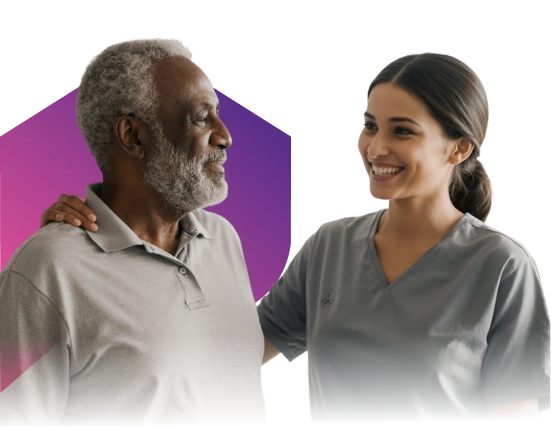 A smiling healthcare worker in gray scrubs warmly supports an older man with gray hair and beard, who is also smiling.