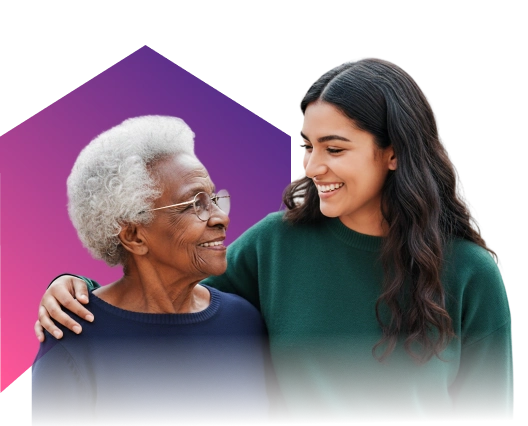 A young woman and an elderly woman share a warm smile, with the young woman’s arm around the elder