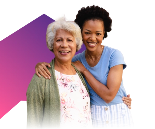A smiling older woman in a floral blouse and cardigan stands next to a younger woman in a blue top.