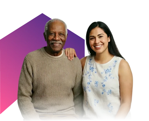 Elderly man in a brown sweater smiles warmly, sitting next to a young woman in a floral blouse who has her arm around his shoulder. Both appear content.