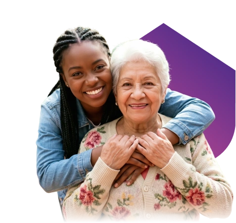 A smiling young woman embraces a cheerful older woman from behind. The older woman wears a floral sweater. The background is black with a purple shape.
