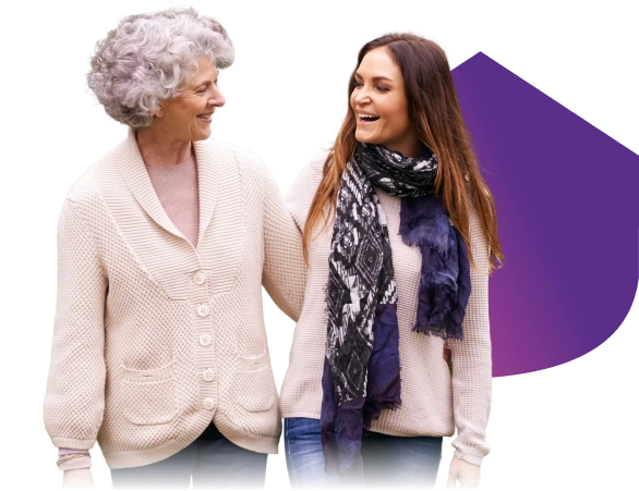 Two women of different ages walking together outdoors and smiling at each other
