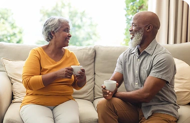 Senior couple sitting on a couch, drinking coffee and talking in a bright living room
