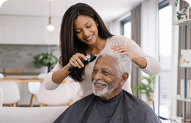 Caregiver cutting an elderly man’s hair in a bright living room