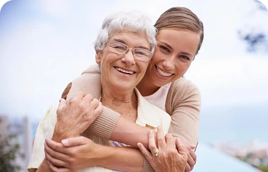 Young woman hugging an elderly woman outdoors near the ocean.