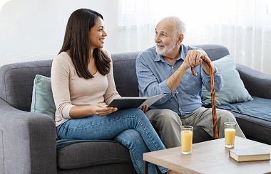 Caregiver comforting an elderly woman with a blanket on a sofa at home